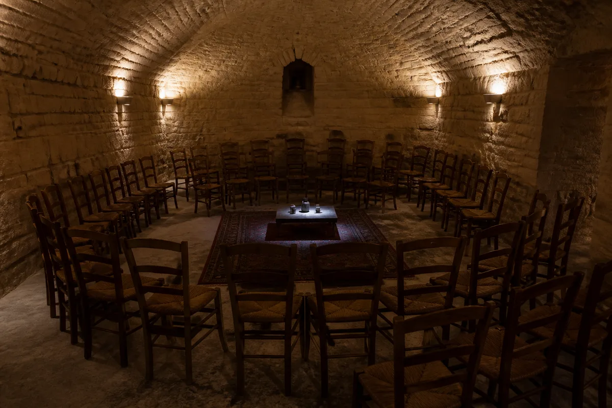 Petite salle voûtée en pierre avec des chaises tournées vers une table basse éclairée