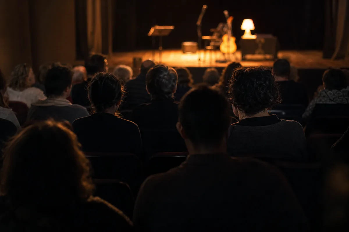 Spectateurs assis de dos dans une petite salle de spectacle, regards tournés vers une scène éclairée