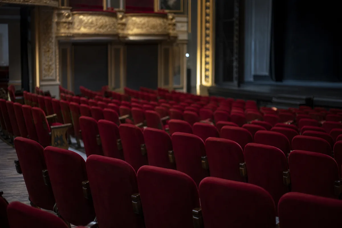 Rangée de fauteuils rouges vides dans un théâtre à l&rsquo;italienne, rampe de scène éteinte